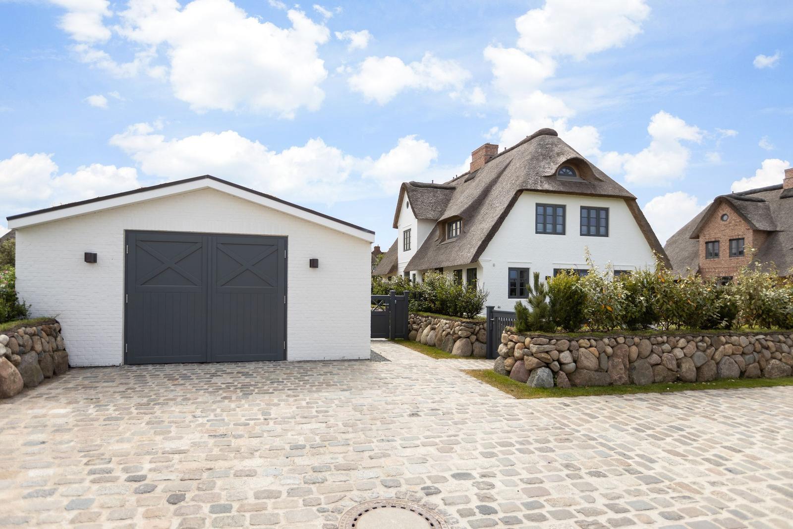 Haus mit Strohdach, weißer Garage und Kiesweg unter blauem Himmel.