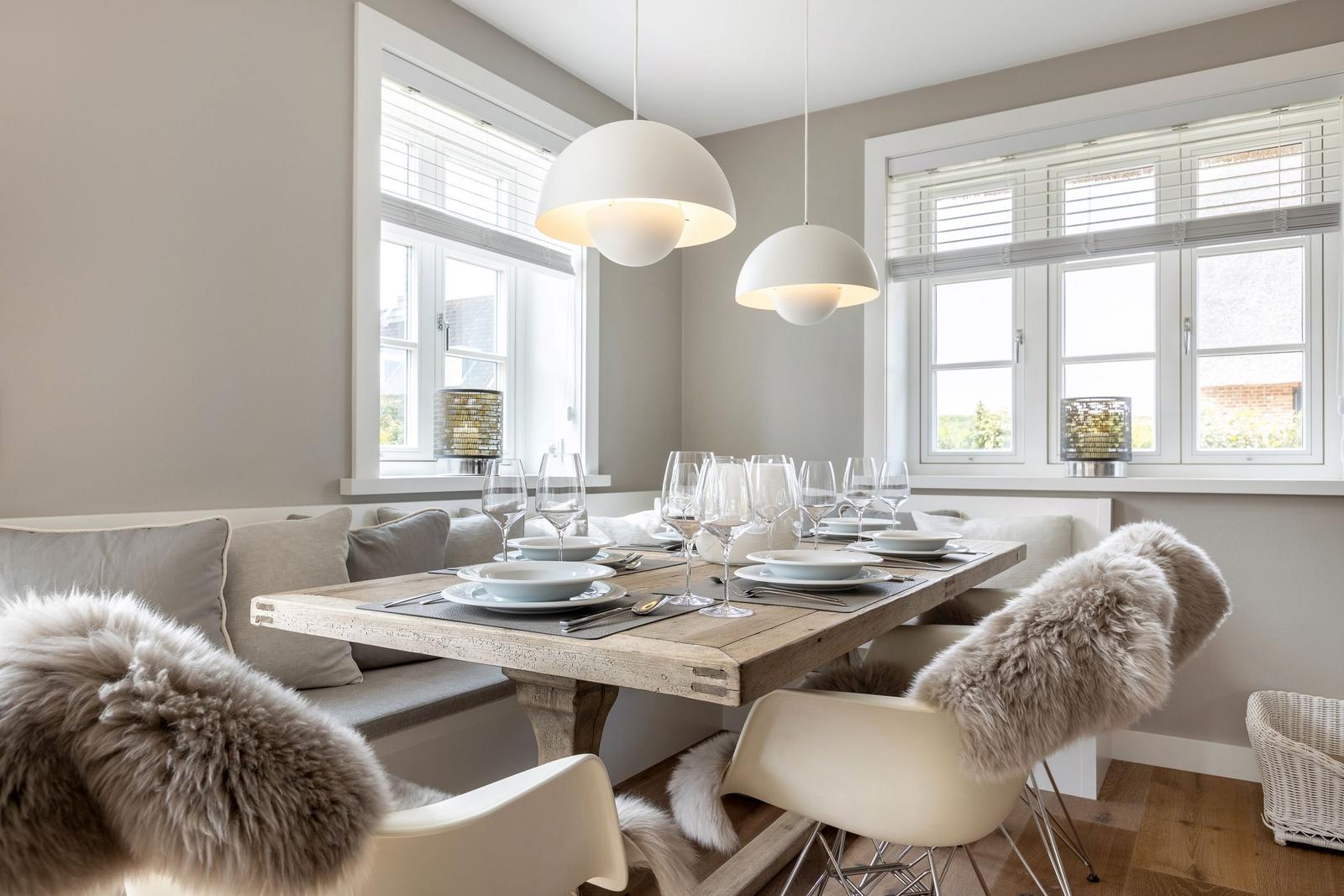 Esszimmer mit Holztisch, weißen Lampen und Fenstern mit Jalousien.