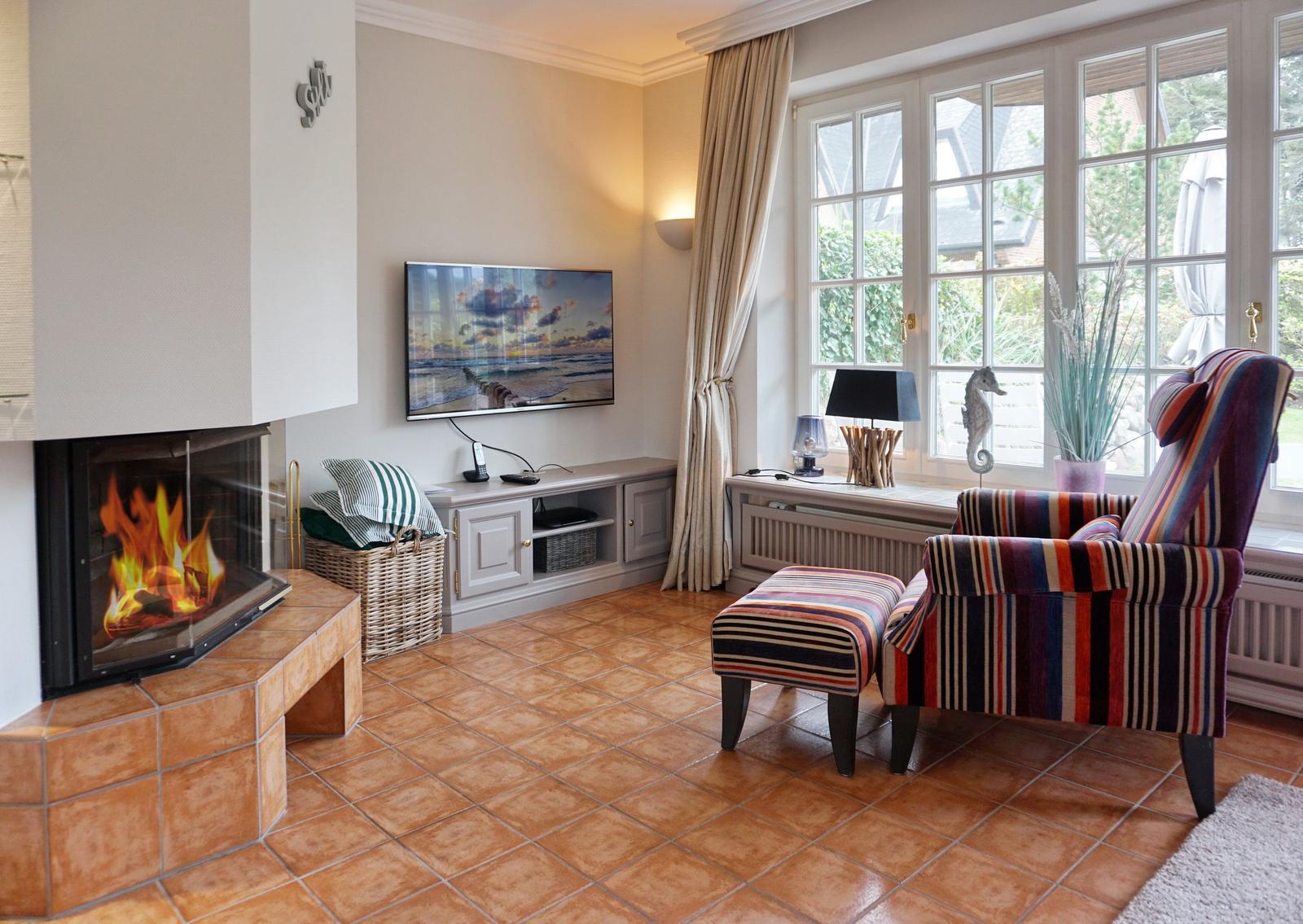 Wohnzimmer mit Kamin, Fernseher und Sessel vor Fenster.