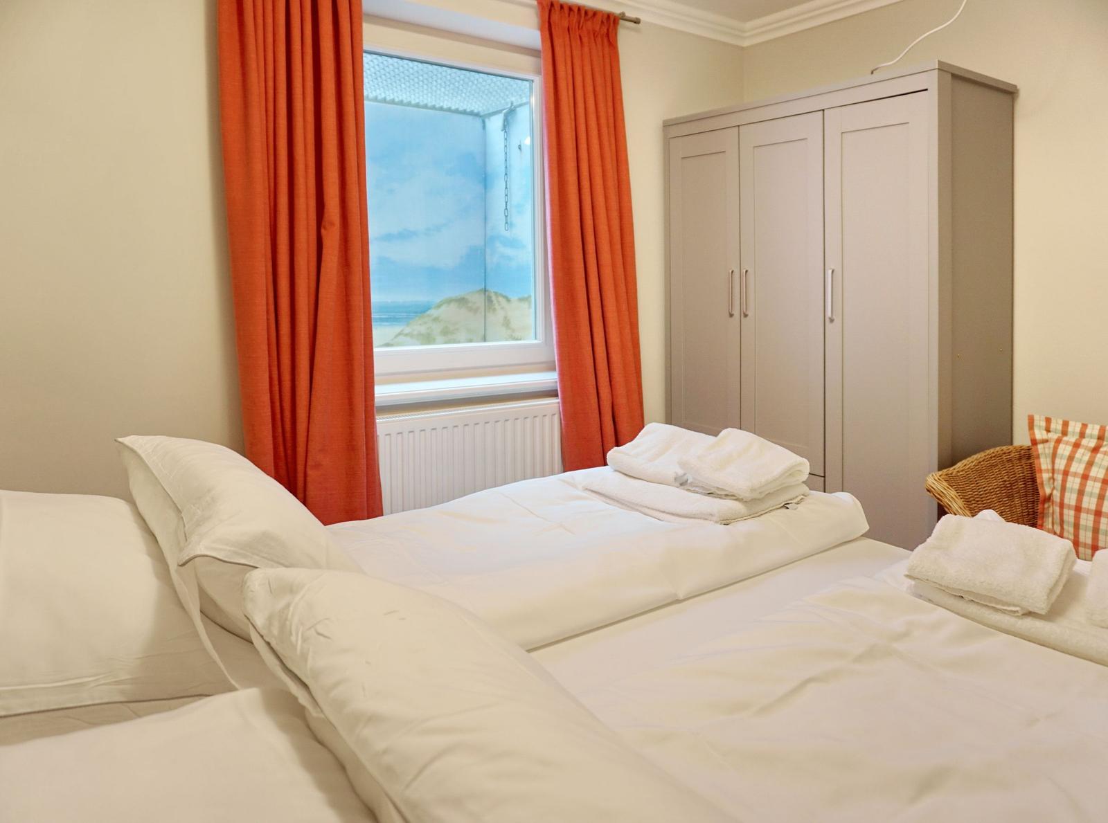 Schlafzimmer mit Bett, Kleiderschrank und Fenster mit Blick auf Strand.