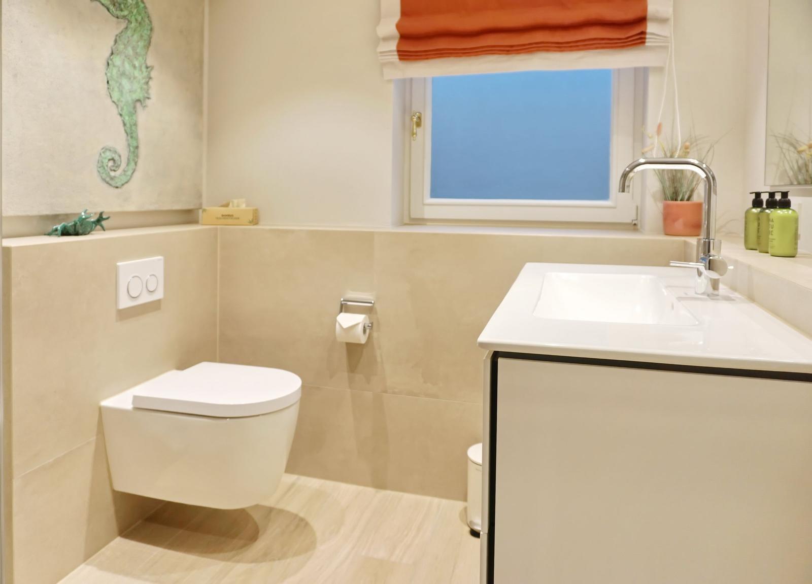 Badezimmer mit Toilette, Waschbecken und Fenster mit orangefarbenem Rollladen.