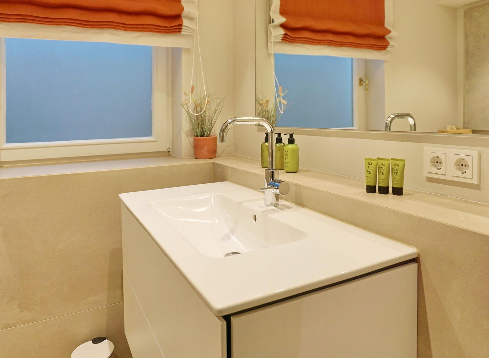 Bad mit Waschbecken, Spiegel und Fenster mit orangefarbenen Rollläden.