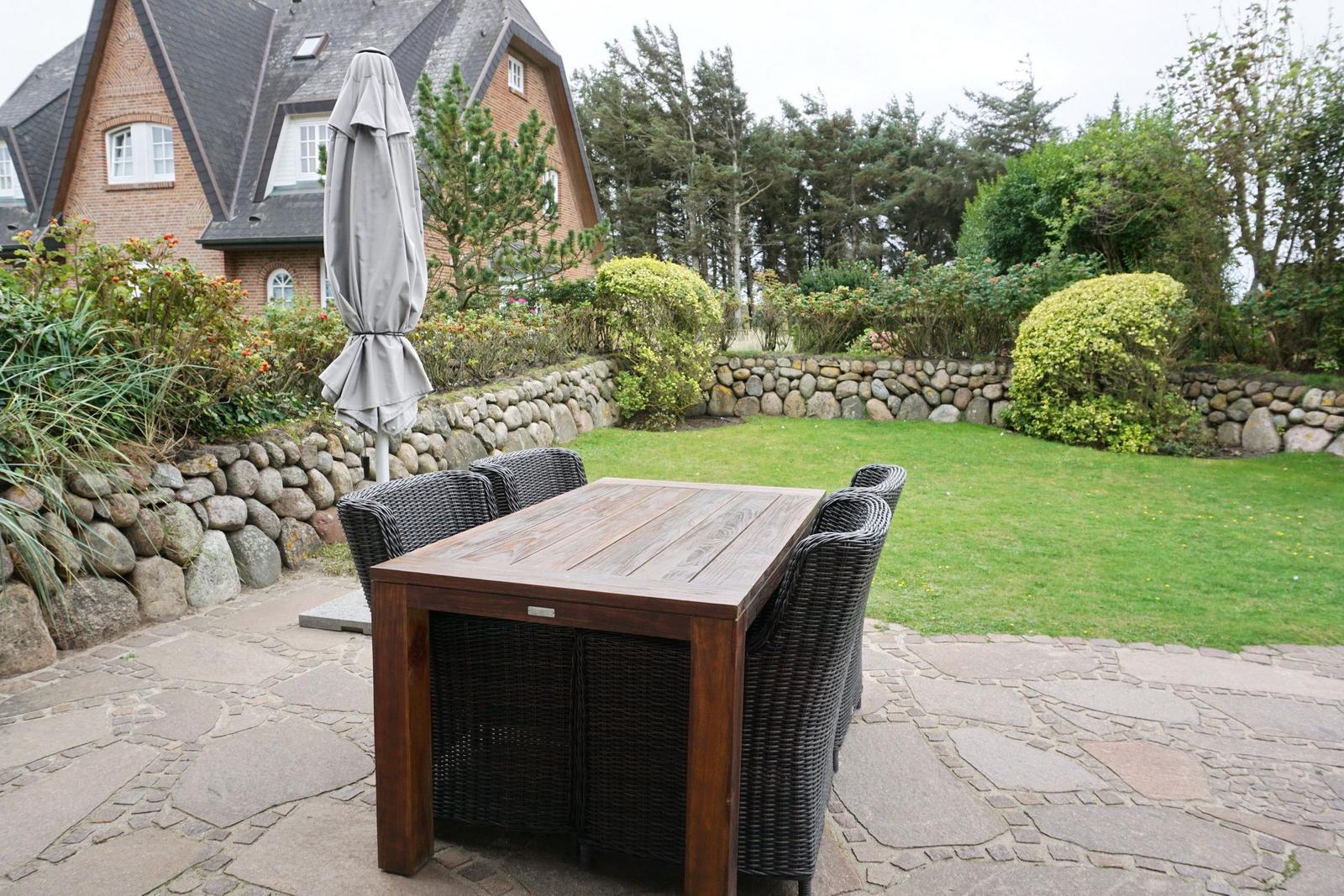 Terrasse mit Tisch und Stühlen, umgeben von Grünfläche und Steinmauer.