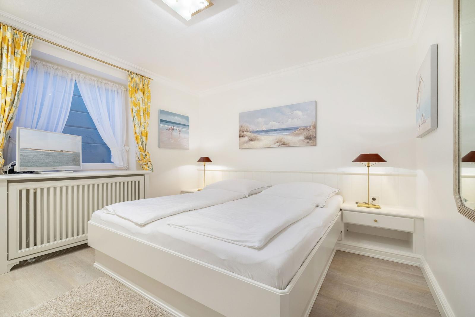 Bedroom with white bed, window, and wall pictures