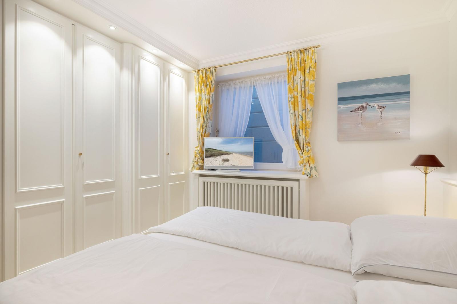 Bedroom with bed, wardrobe, and window with yellow curtains.