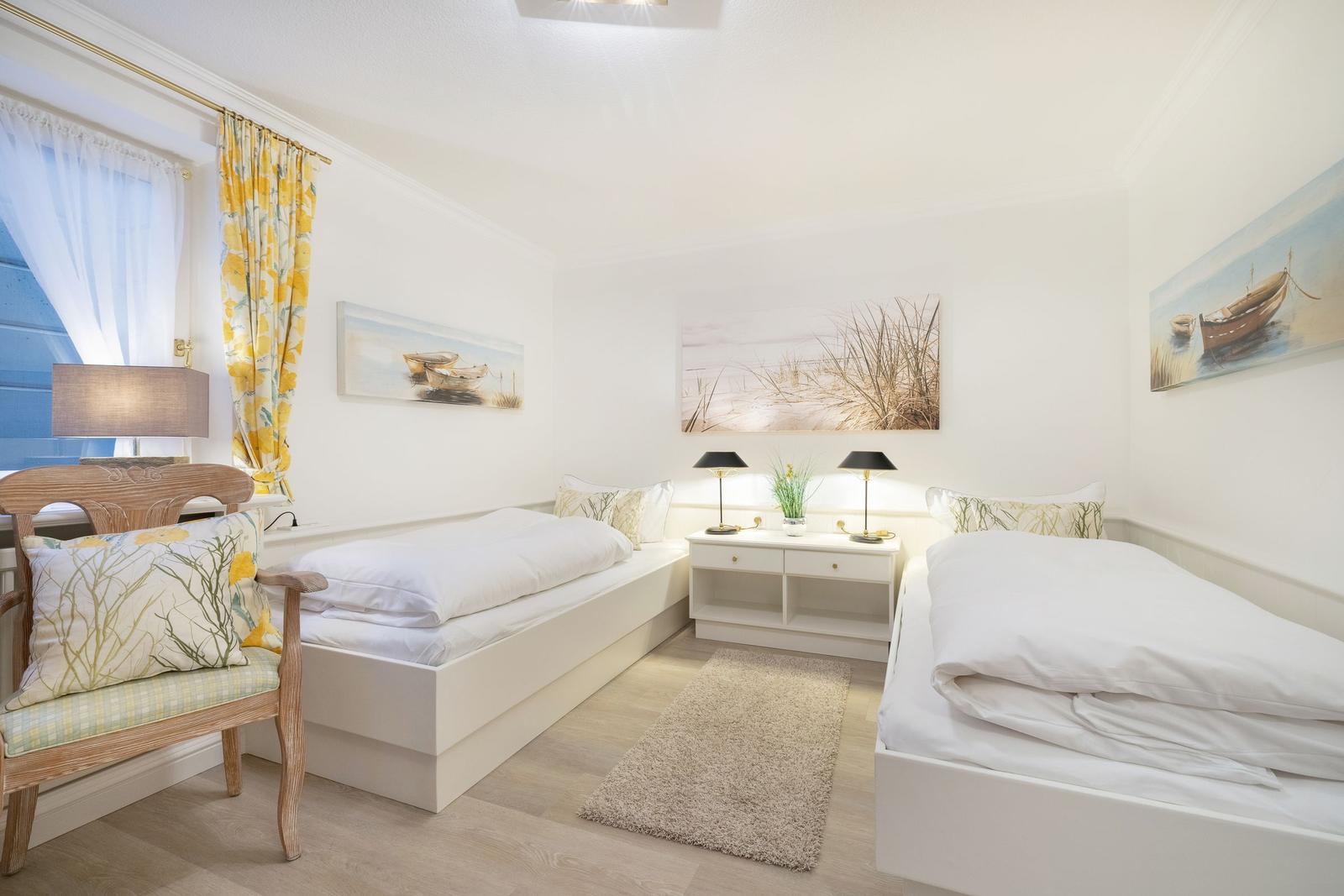 Two beds, nightstands with lamps, and window with yellow curtains.