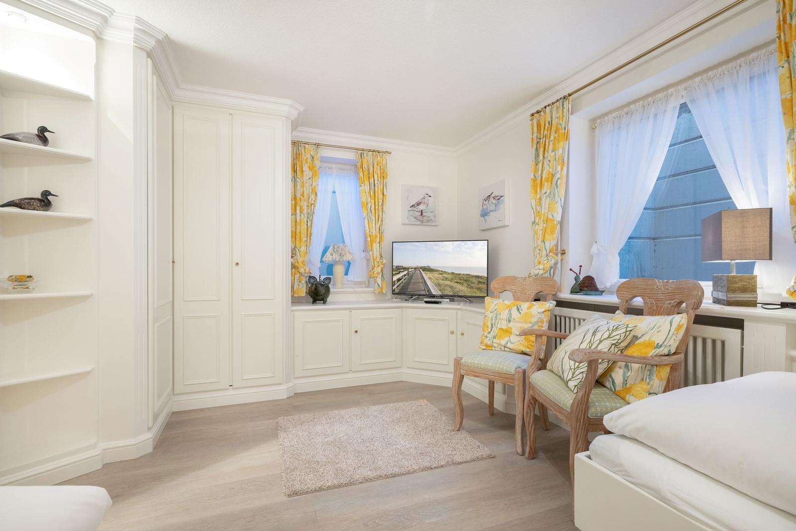 Room with white cabinets, windows with yellow curtains, and a TV.