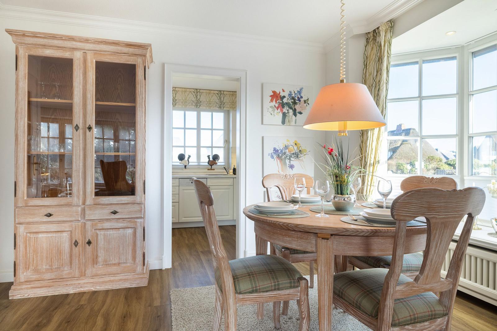 Dining room with wooden table, chairs, and glass cabinet. View of kitchen and thatched roofs.