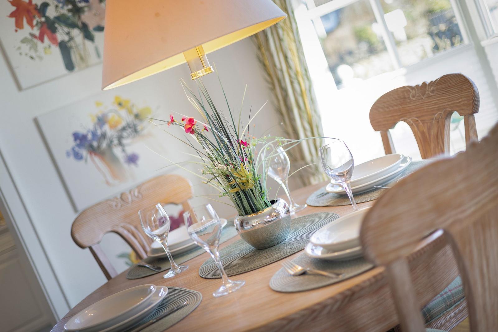 Set dining table with chairs, placemats, glasses, and flower vase.