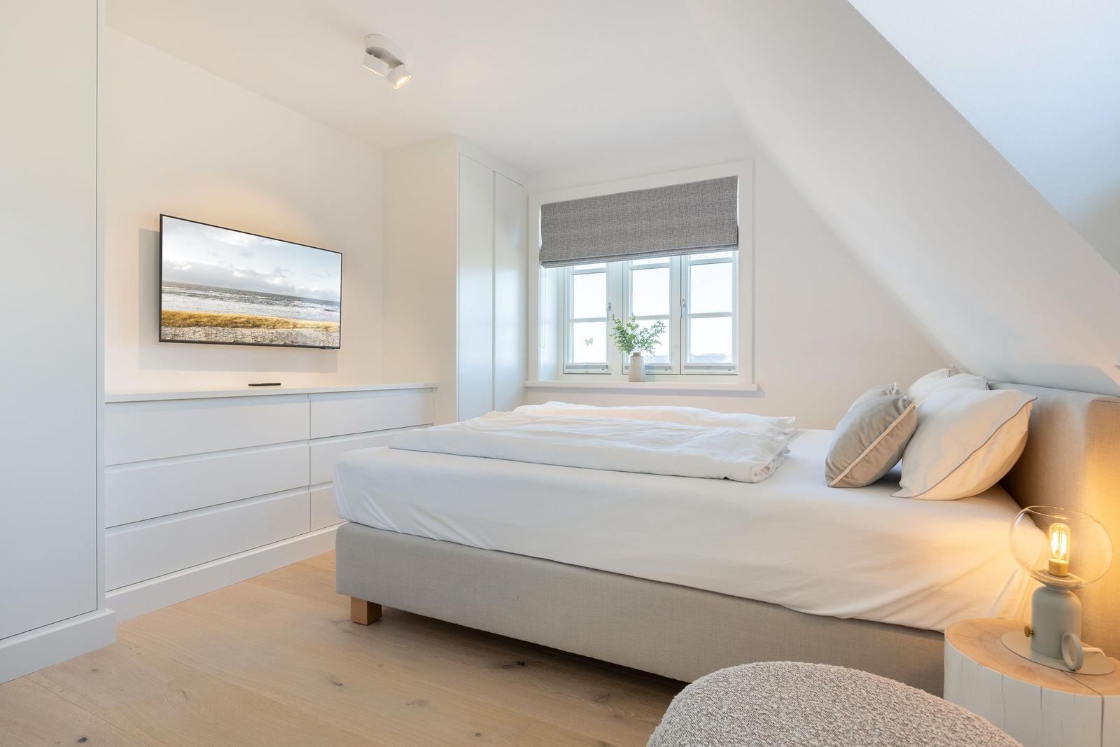 Bedroom with bed, window, and TV mounted on the wall.