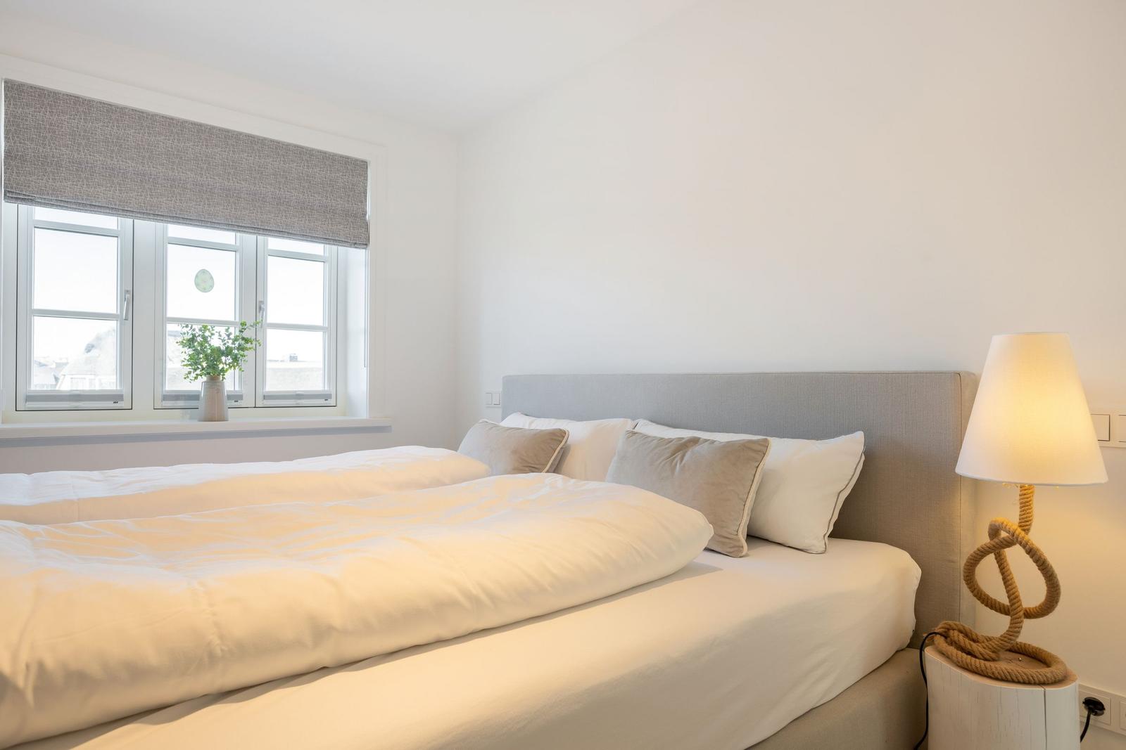 Bedroom with bed, window, and standing lamp.