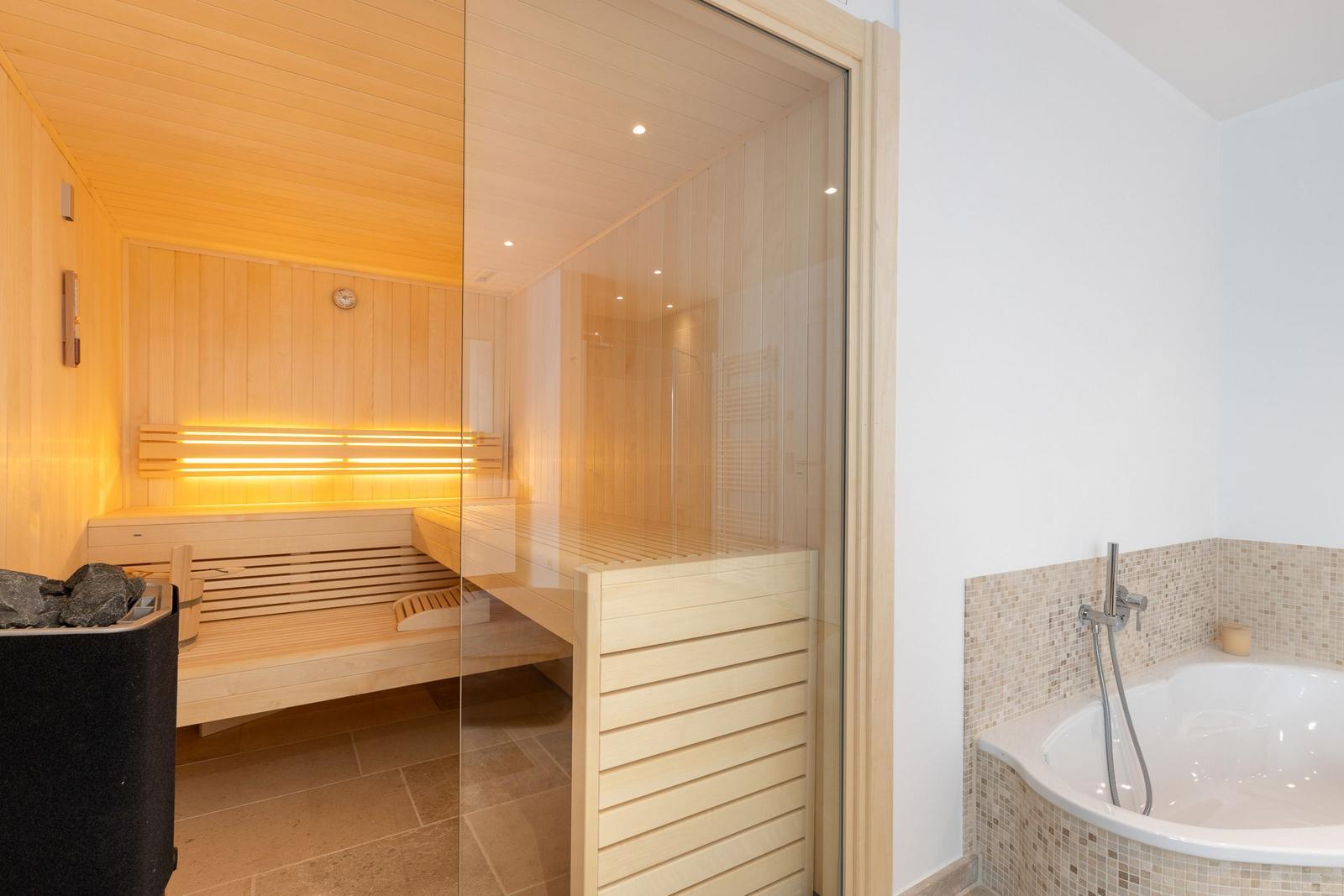 Sauna with wooden bench and bathtub with mosaic tiles