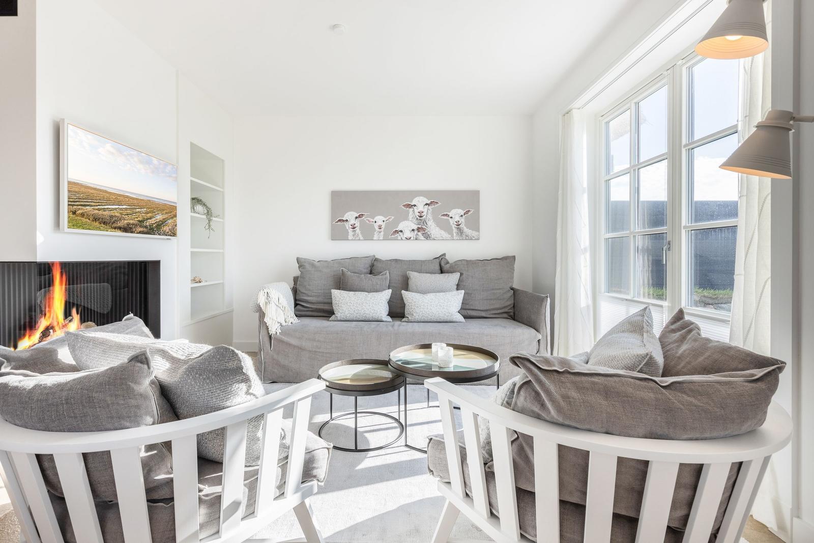 Living room with fireplace, sofa, and two chairs. Pictures hang on the walls.