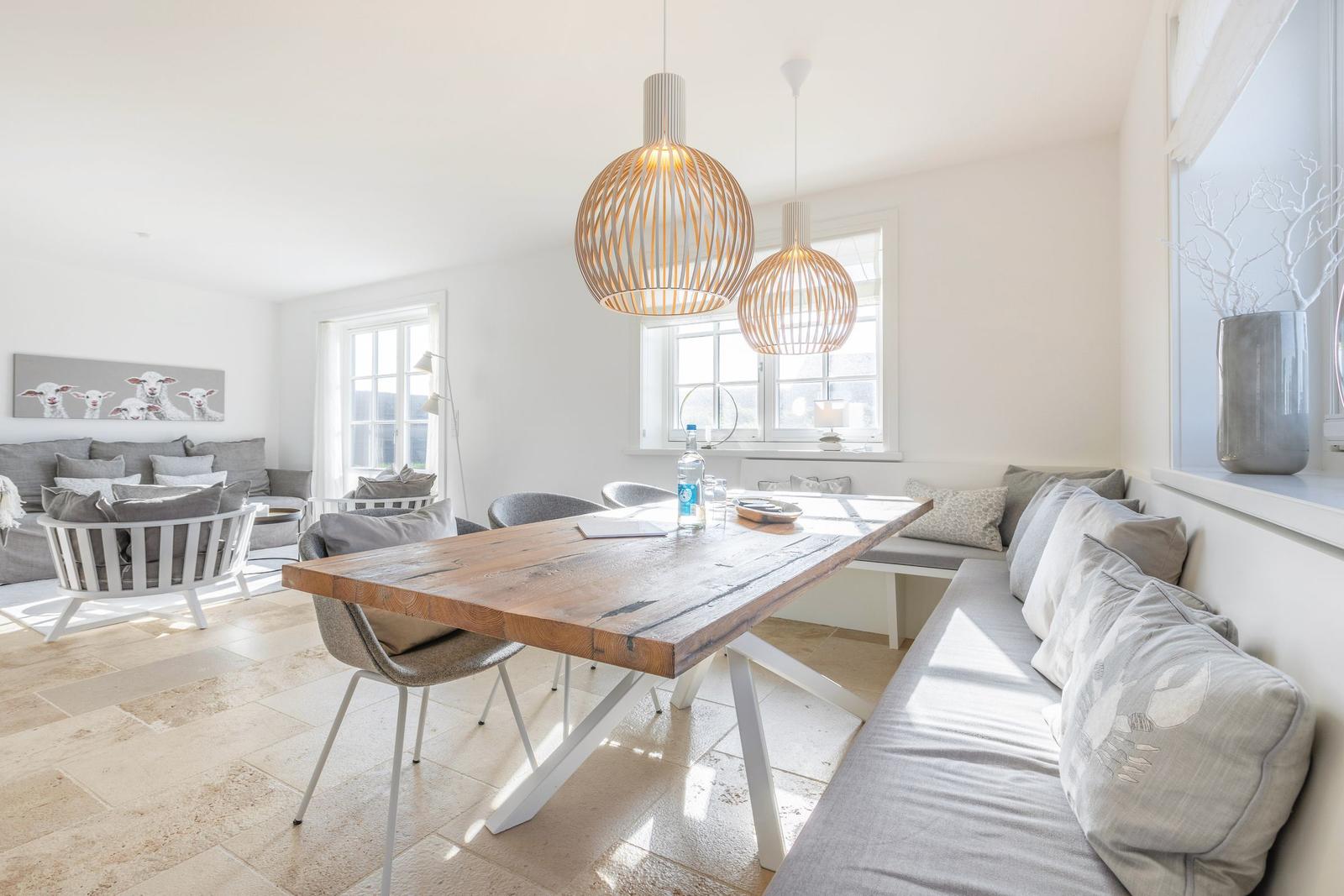 Dining area with wooden table, bench, and pendant lamps. Living area with sofa and wall art.