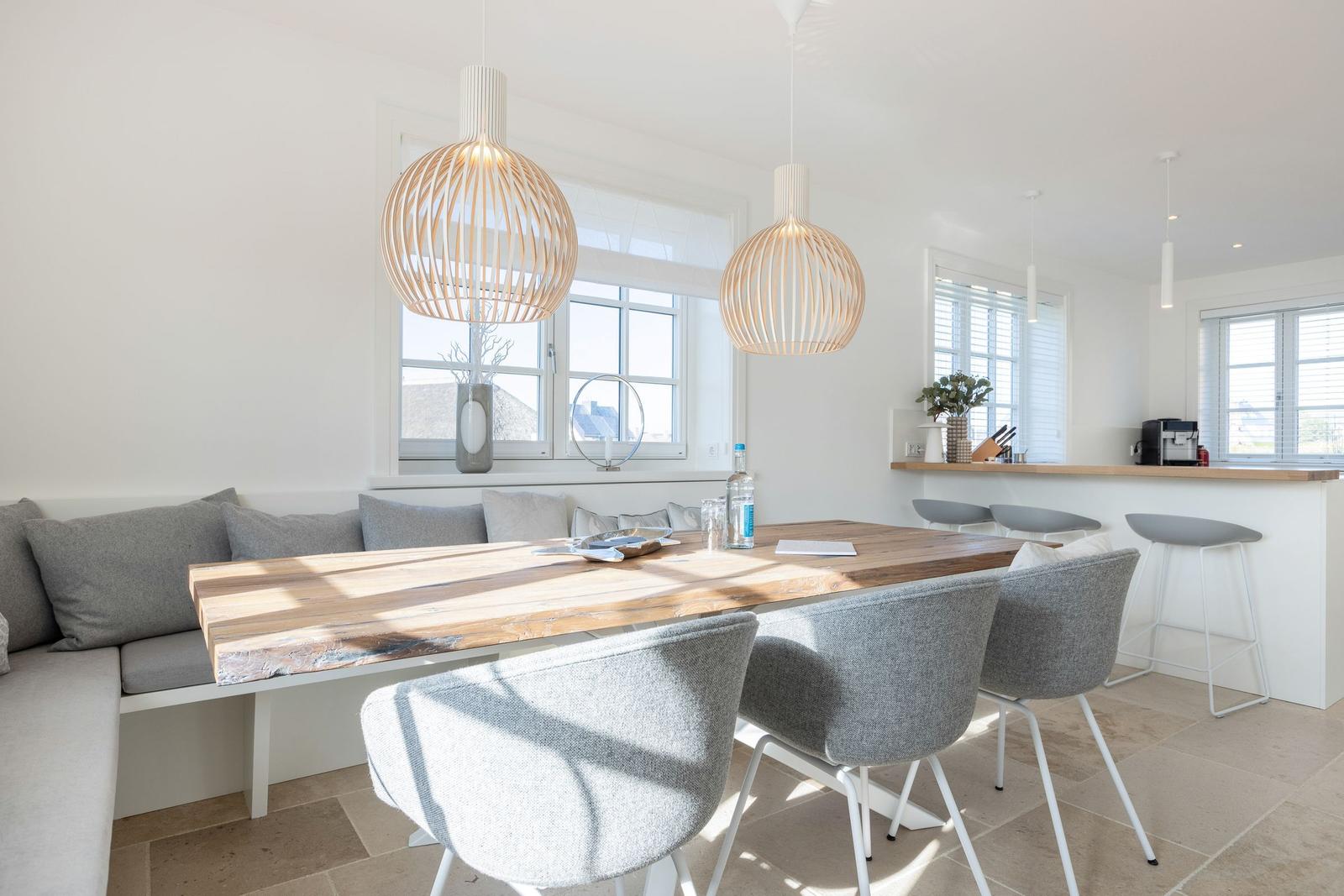 Dining area with wooden table, gray chairs, and bench. Two pendant lights and windows with view.