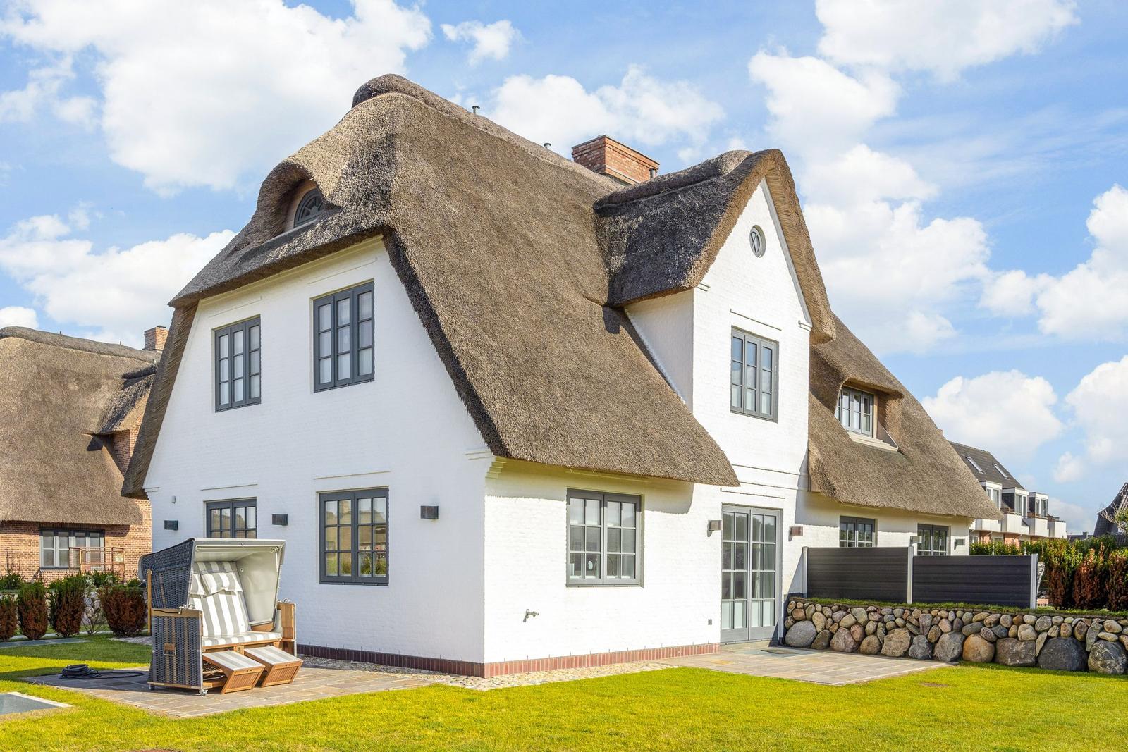 House with thatched roof and white facade. Garden area with sun lounger.