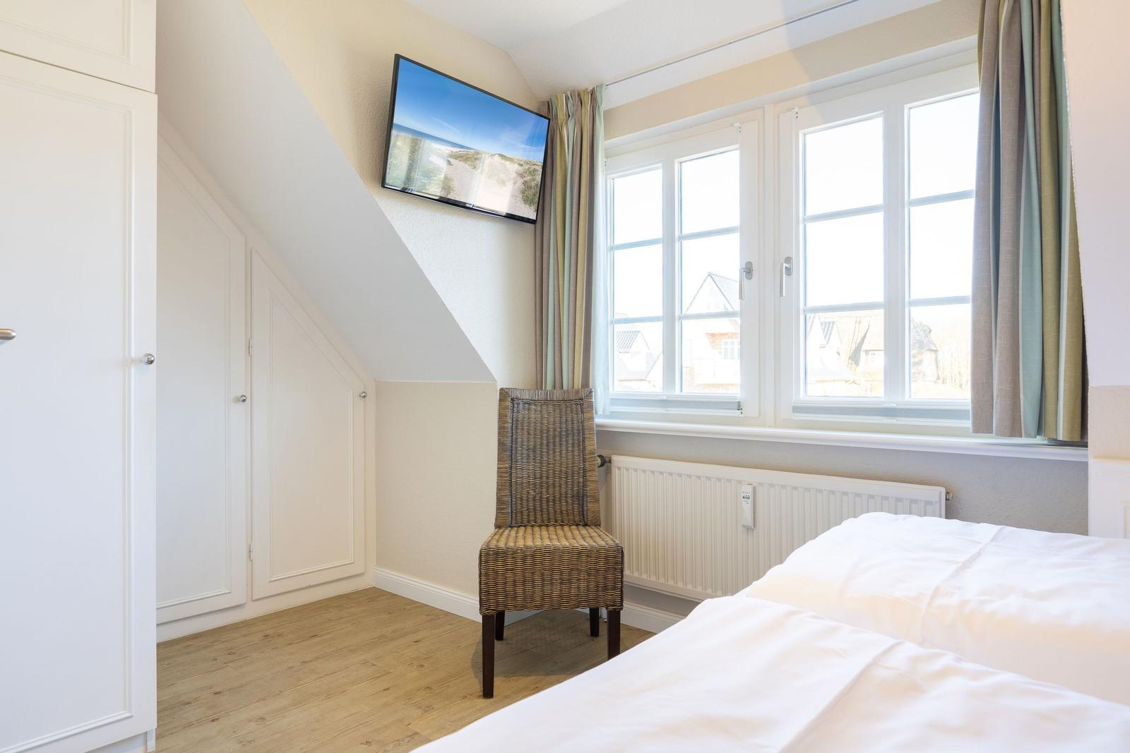 Bedroom with sloped ceiling, bed, chair, and TV.