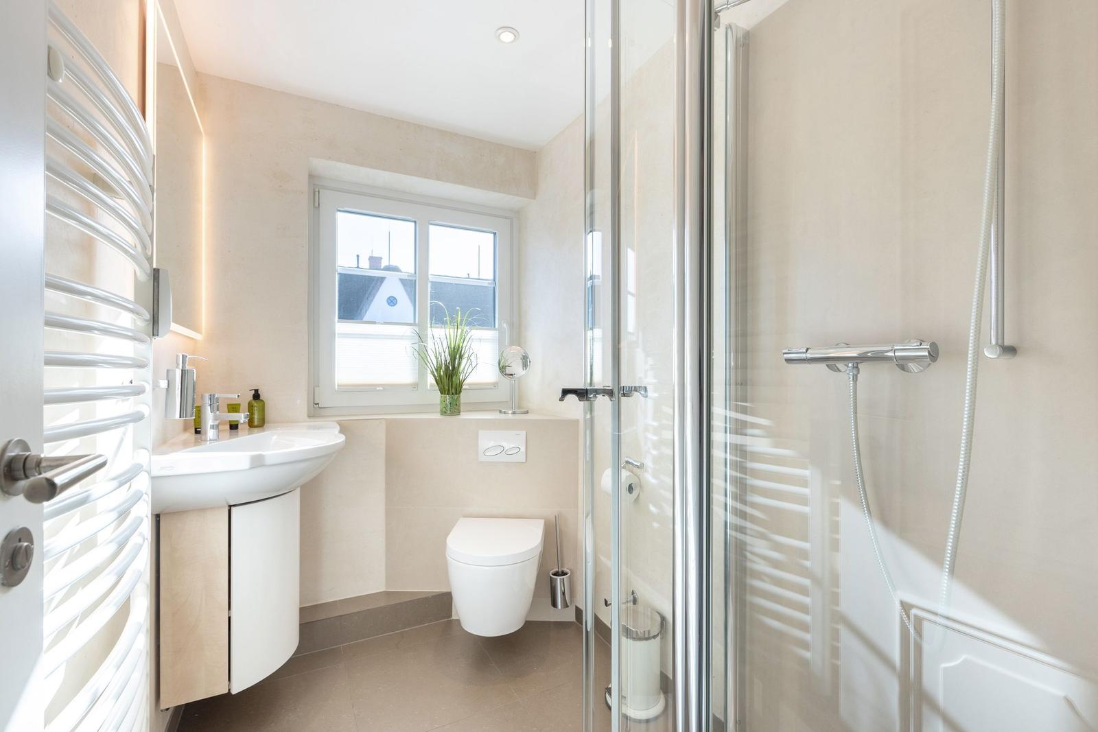 Bathroom with shower, sink, and toilet. Window with plant.