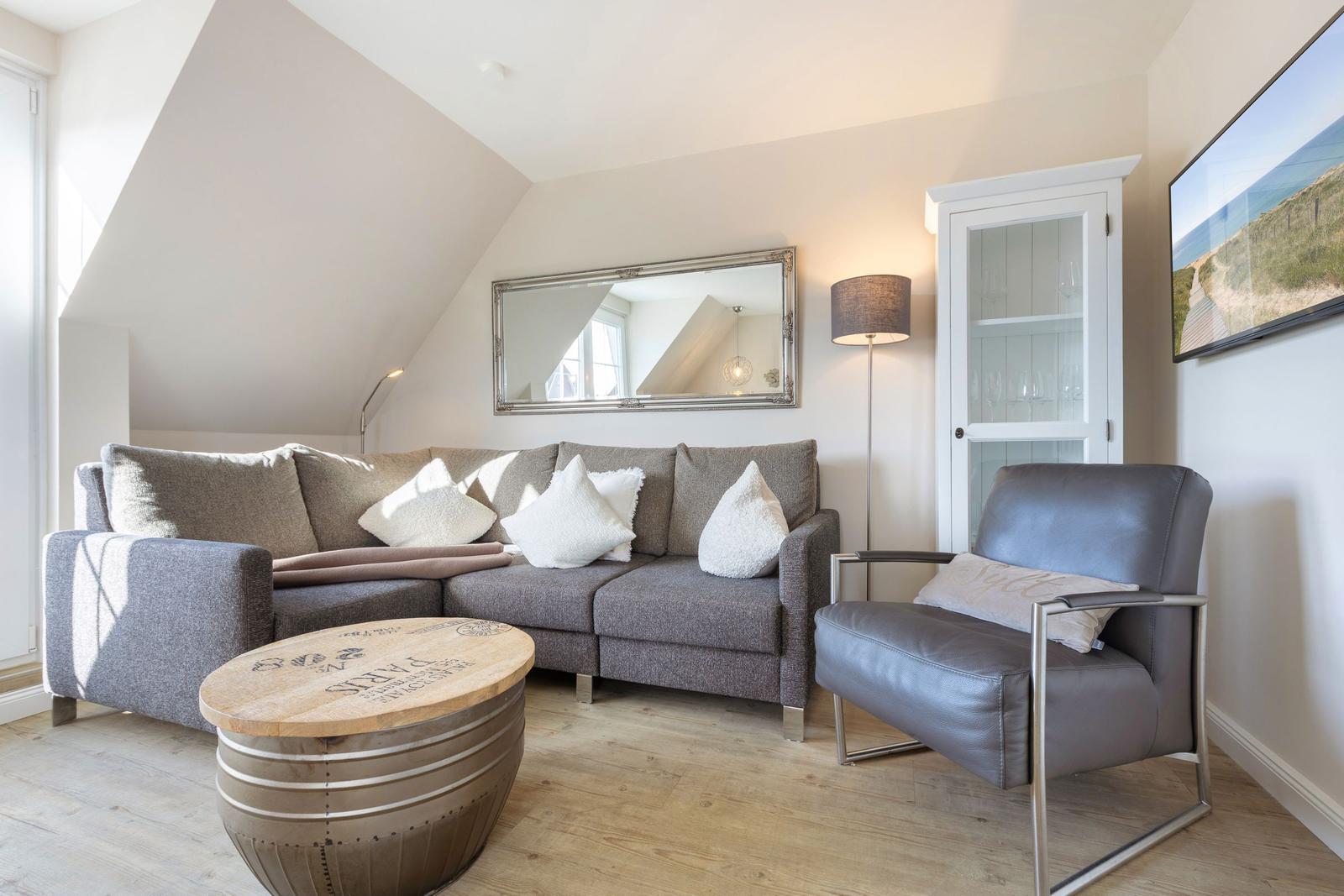 Living room with gray sofa, leather armchair, and wooden table under sloped ceiling.