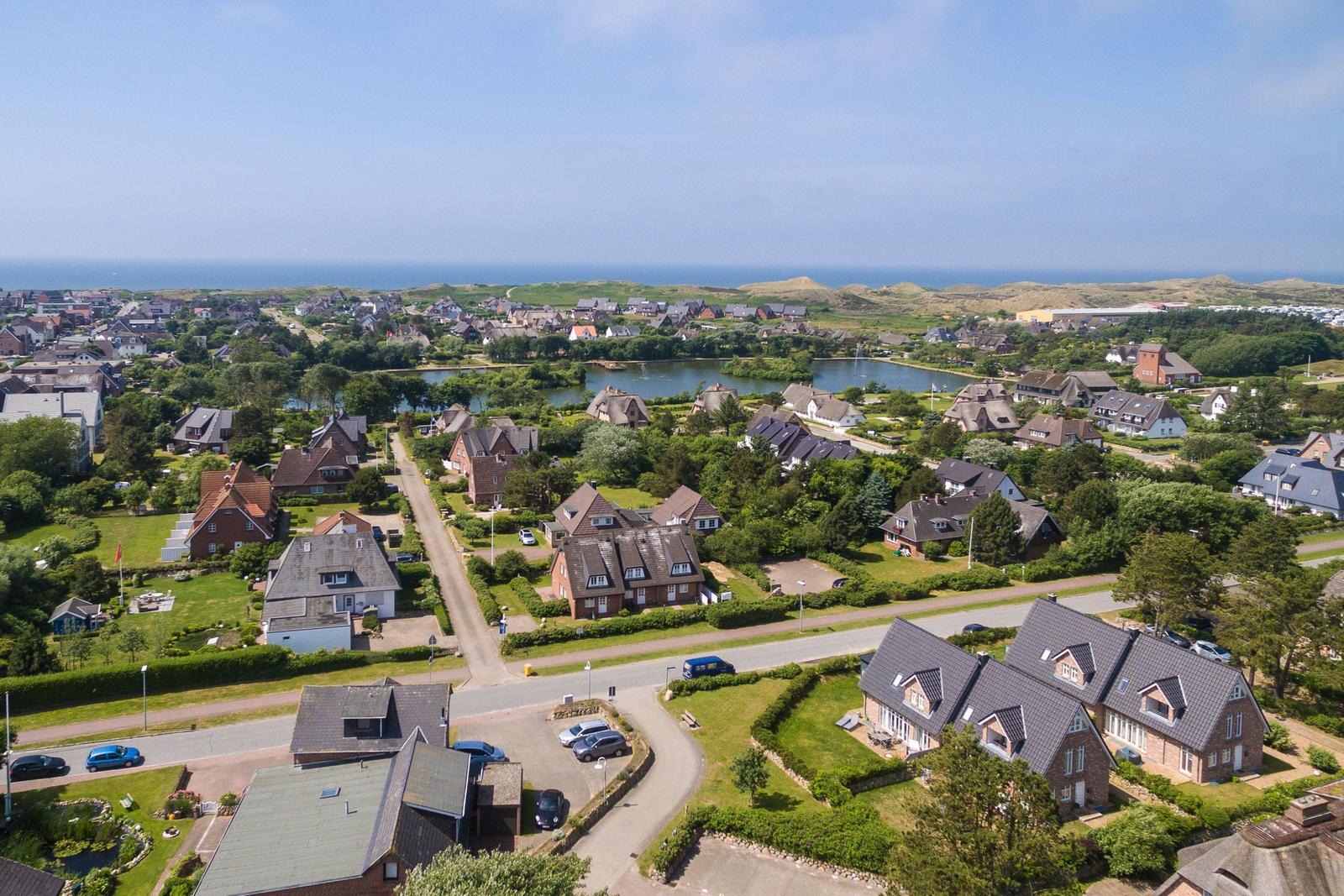 Aerial view of a village with houses, greenery, and a lake near the sea.