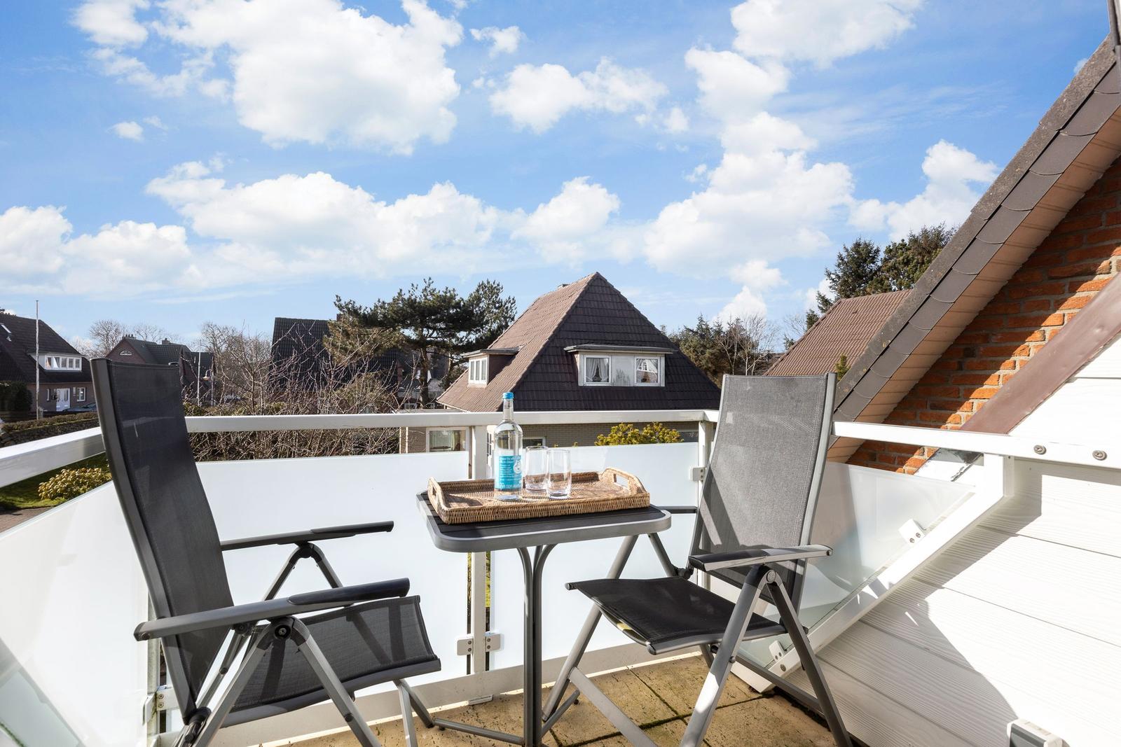 Terrace with two chairs and table. Background: houses and blue sky.