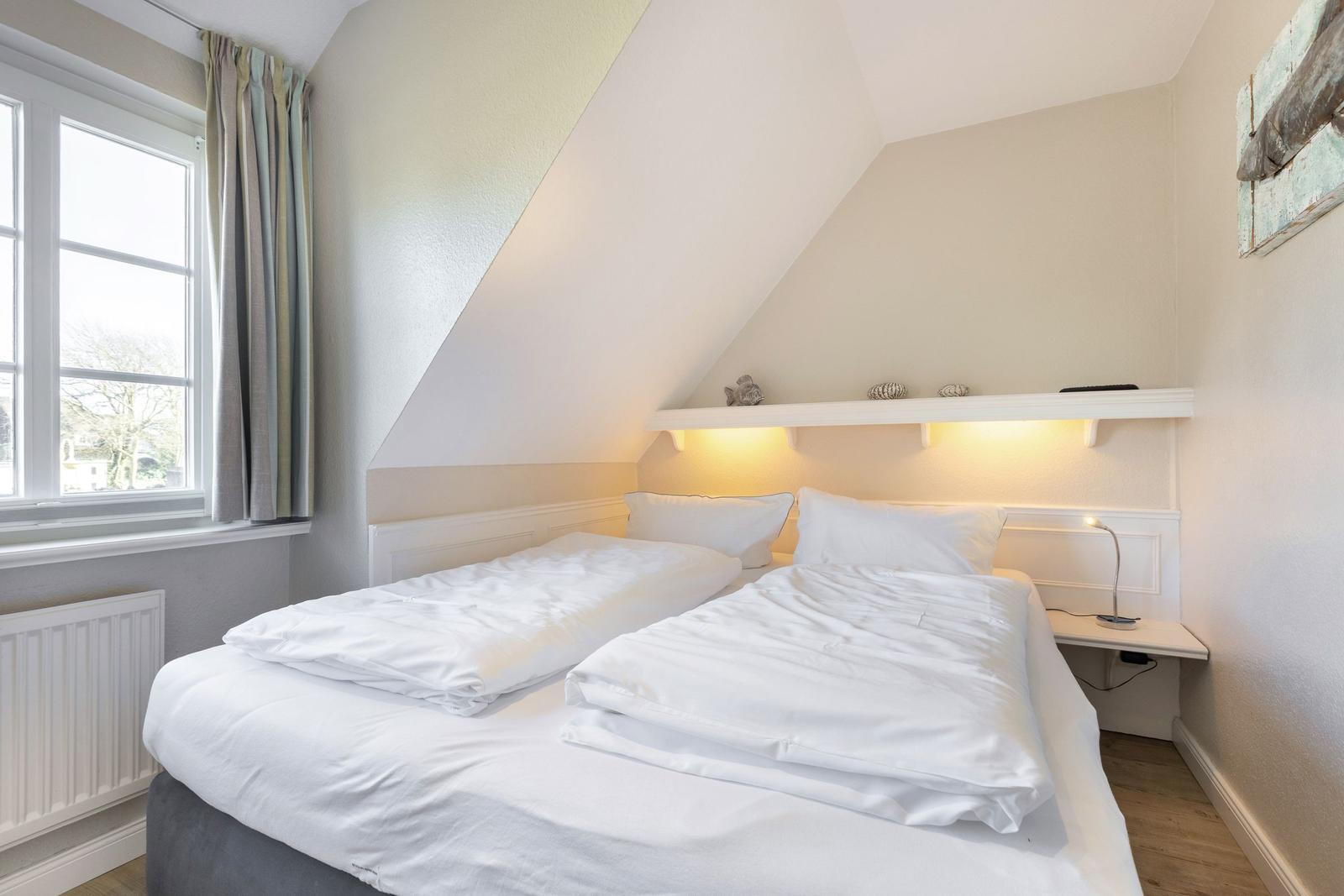 Room with double bed, window, and floating desk under sloped ceiling.