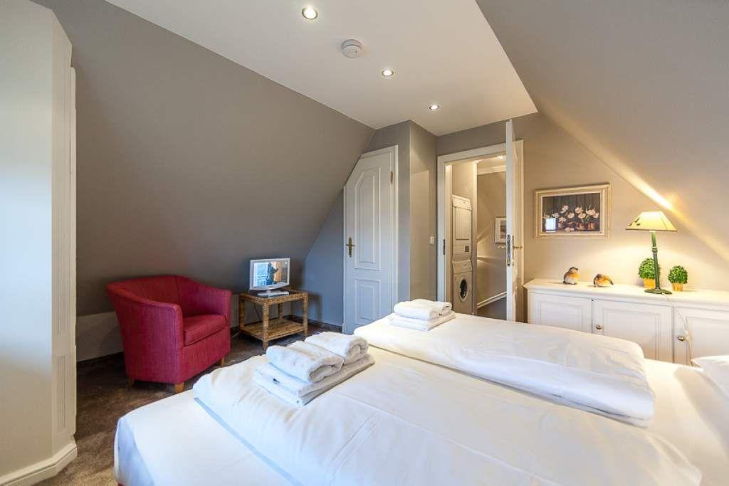 Bedroom with double bed, red armchair, and wardrobe. Door leads to bathroom.