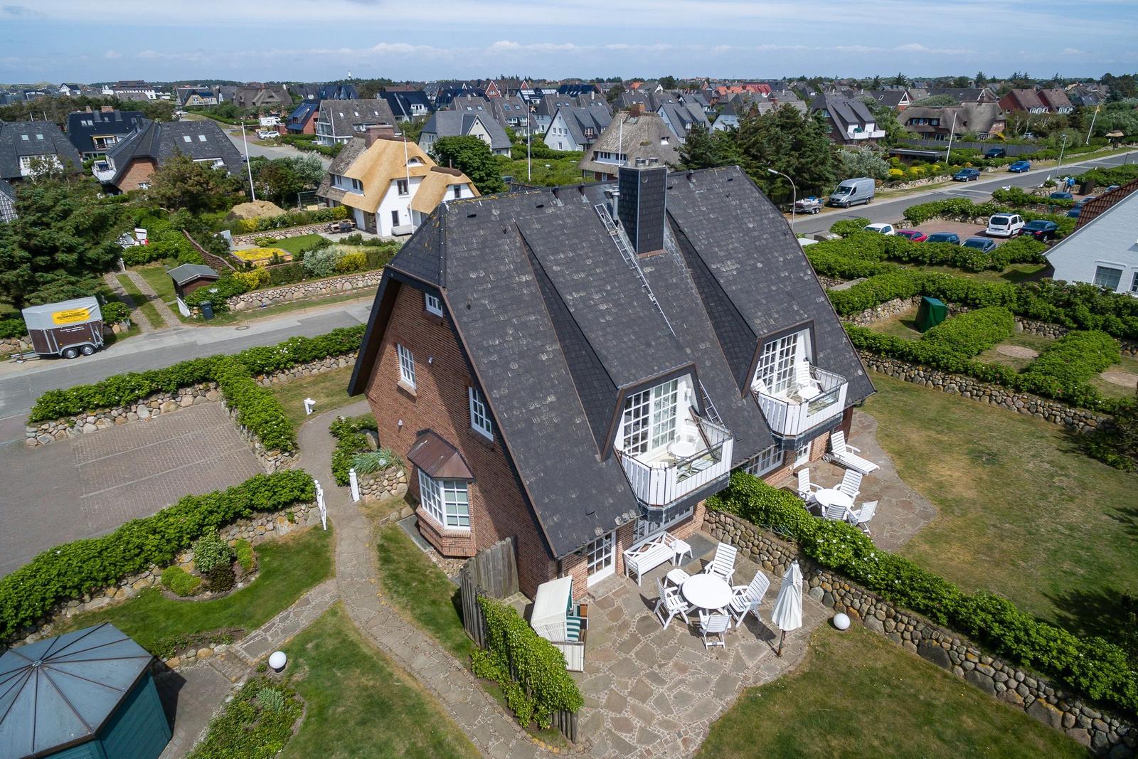 House with balcony, terrace, and garden. Surrounded by greenery and neighboring houses.
