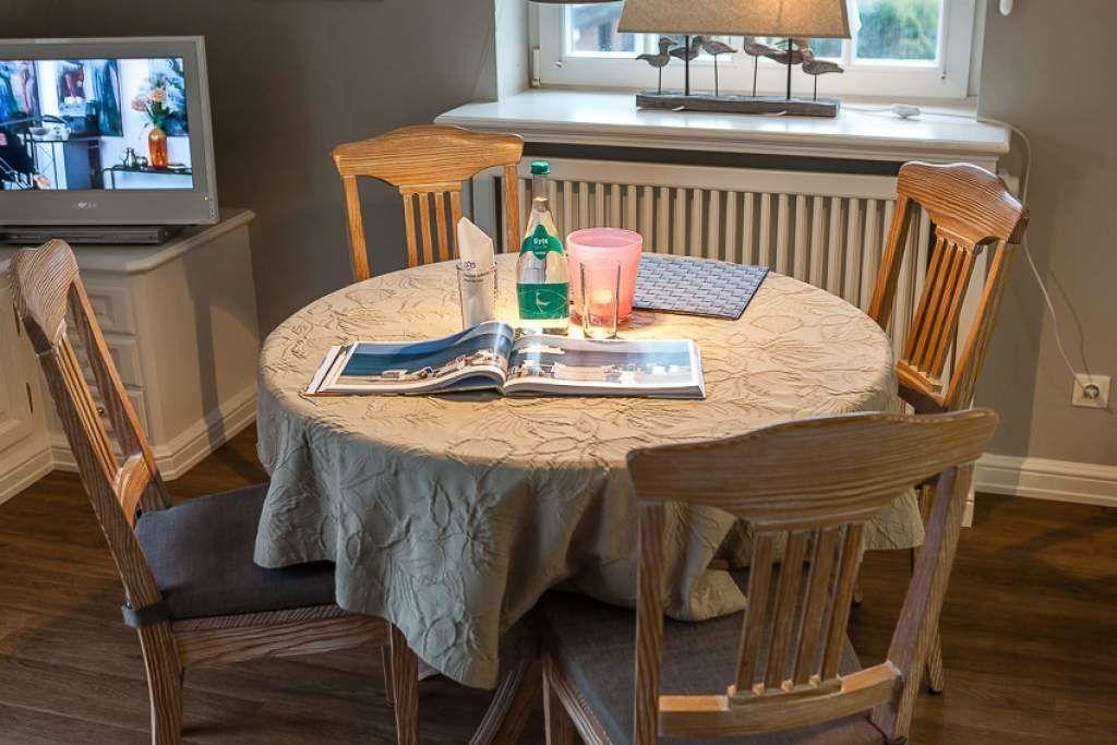 Round table with four chairs, tablecloth, magazines, and drinks.