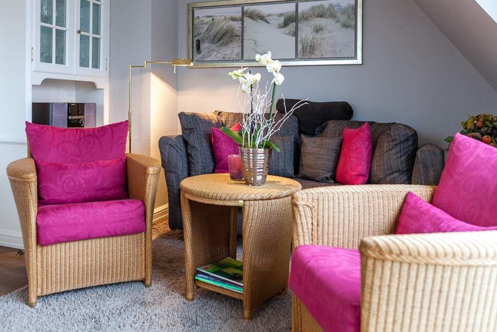 Living room with rattan furniture and pink cushions. Wall art shows dunes.