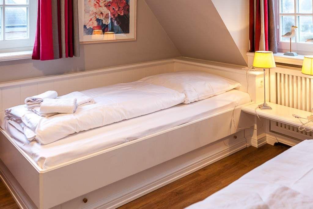 A bed with white linens, nightstand, and window with curtains.