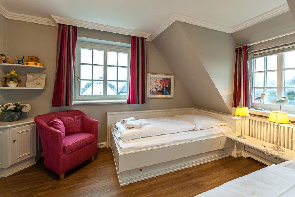 Bedroom with sloped ceiling, two windows, and a red armchair.