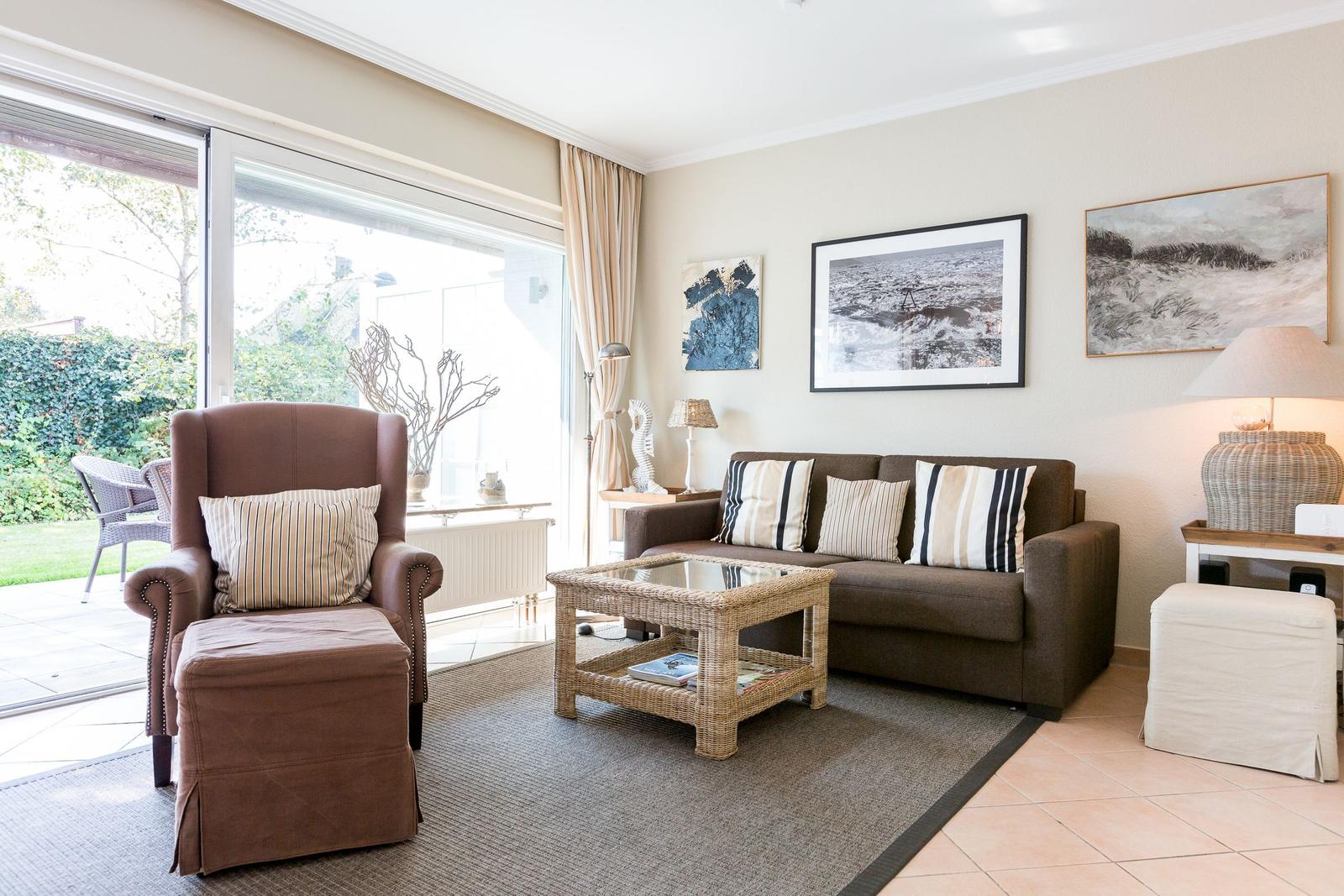 Living room with brown sofa, armchair, and glass coffee table. Large sliding door to garden.