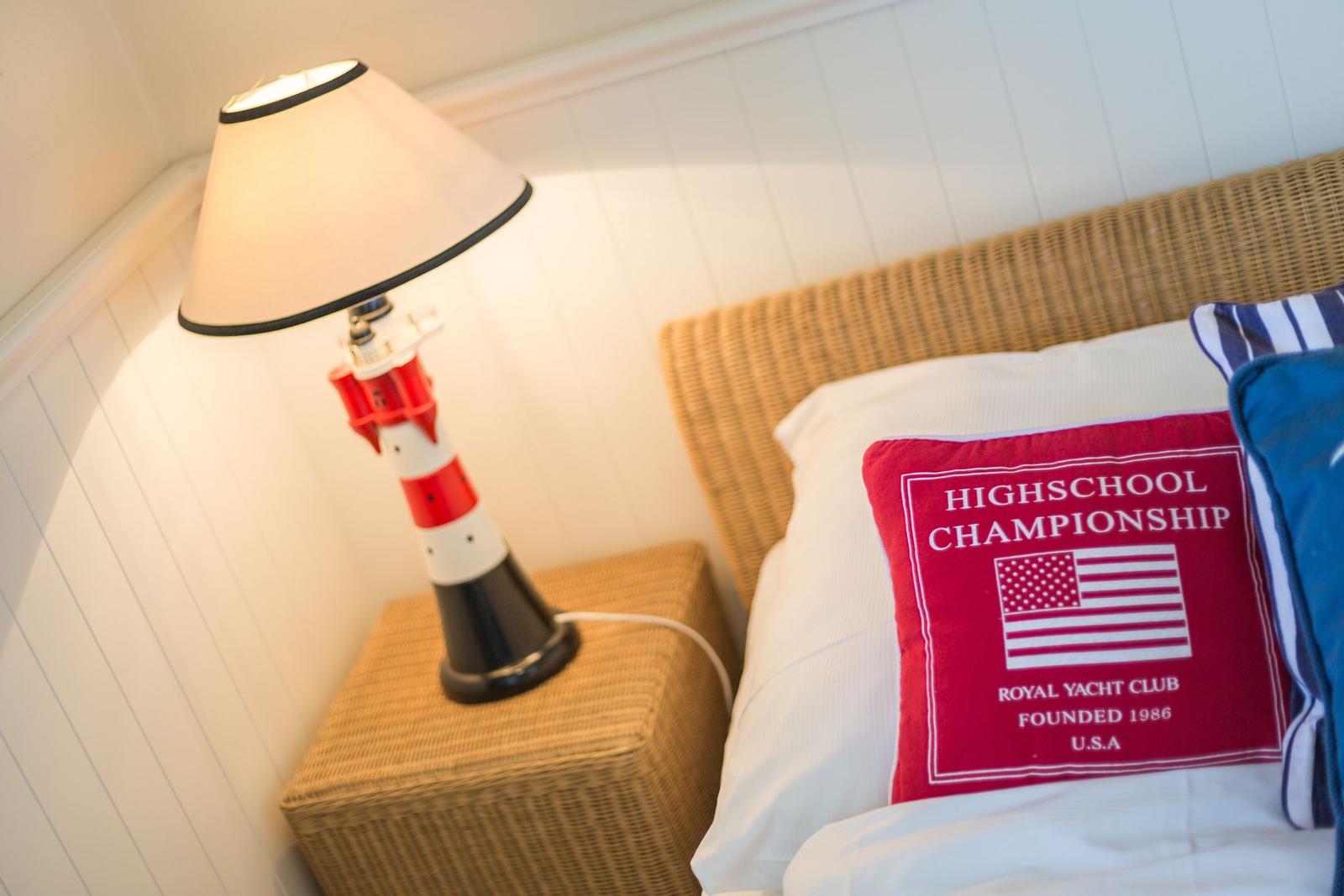 Bedroom with lighthouse lamp, pillow, and wicker headboard.