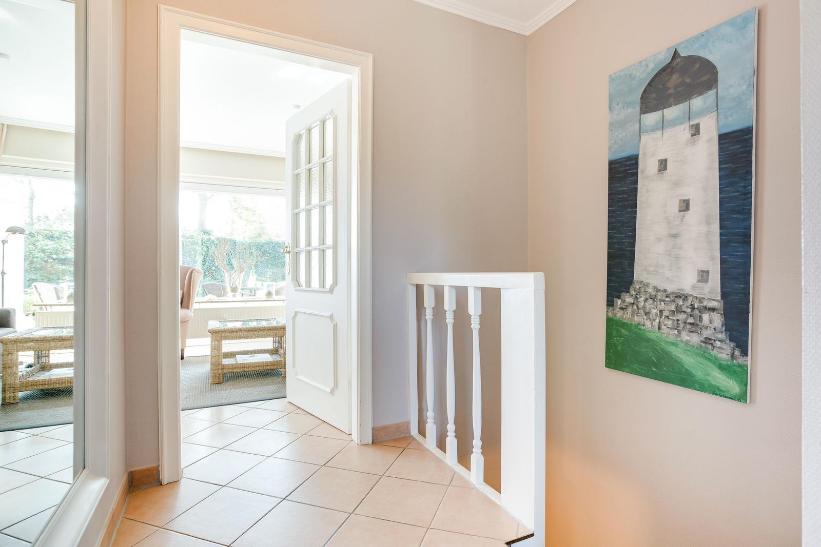 Hallway with staircase railing and lighthouse painting on the wall.