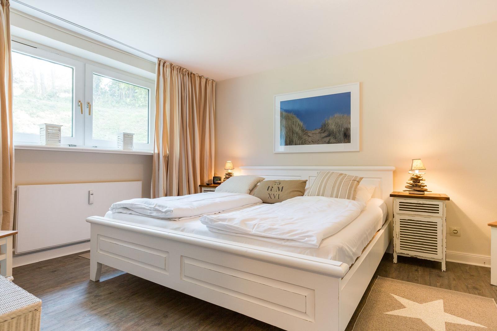 Bedroom with white bed, window, and picture on the wall.