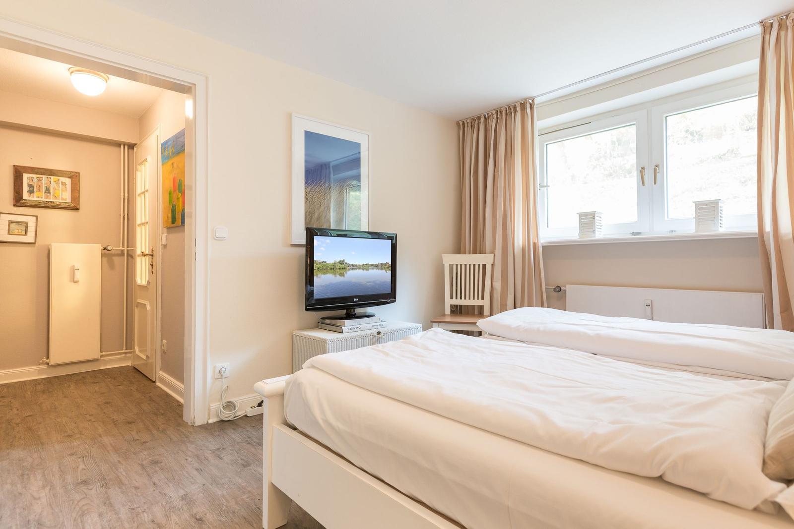 Bedroom with bed, TV, and window with curtains.