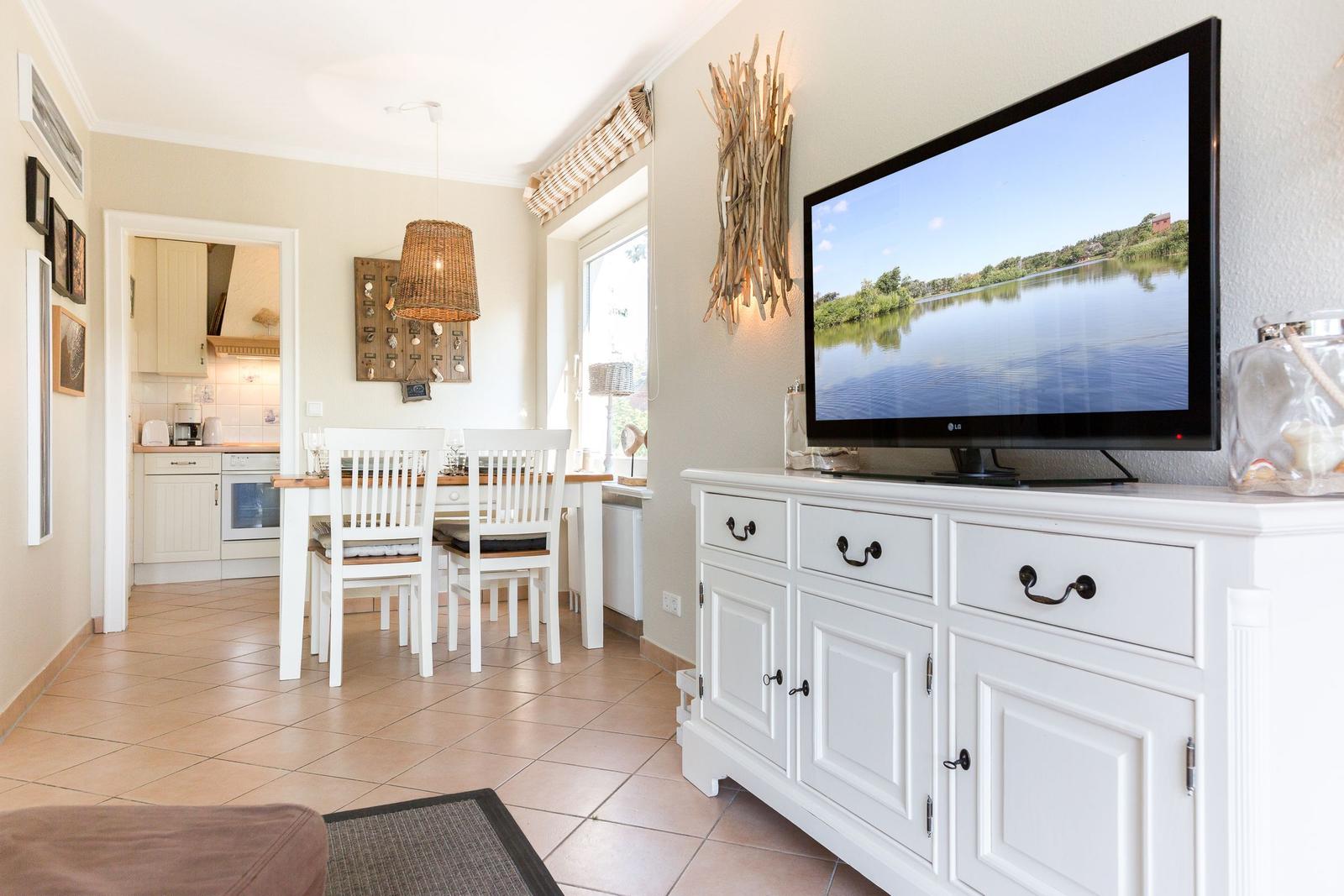 Living room with TV, dining table, and kitchen area in background.