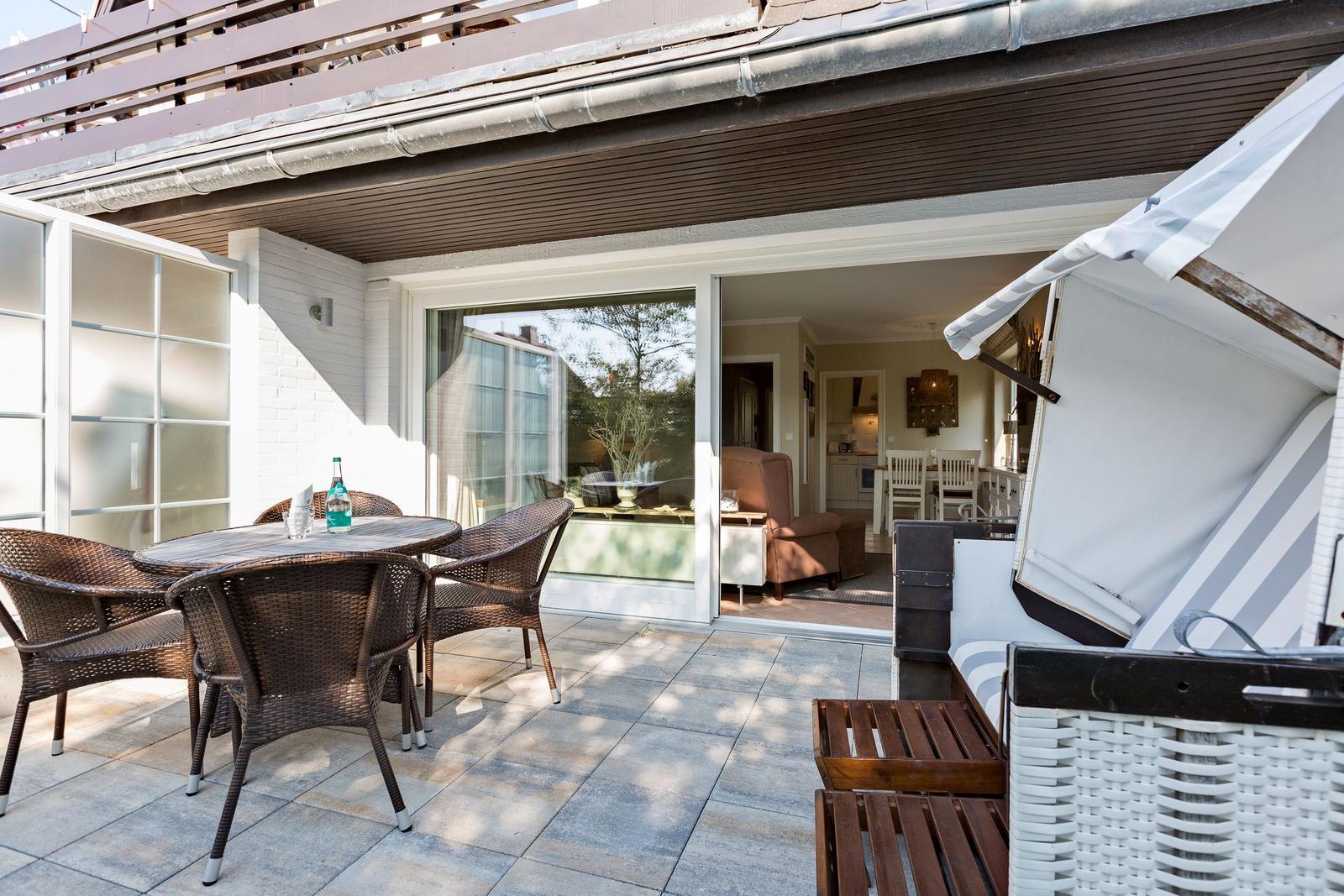 Terrace with table and chairs, view into house with seating area.