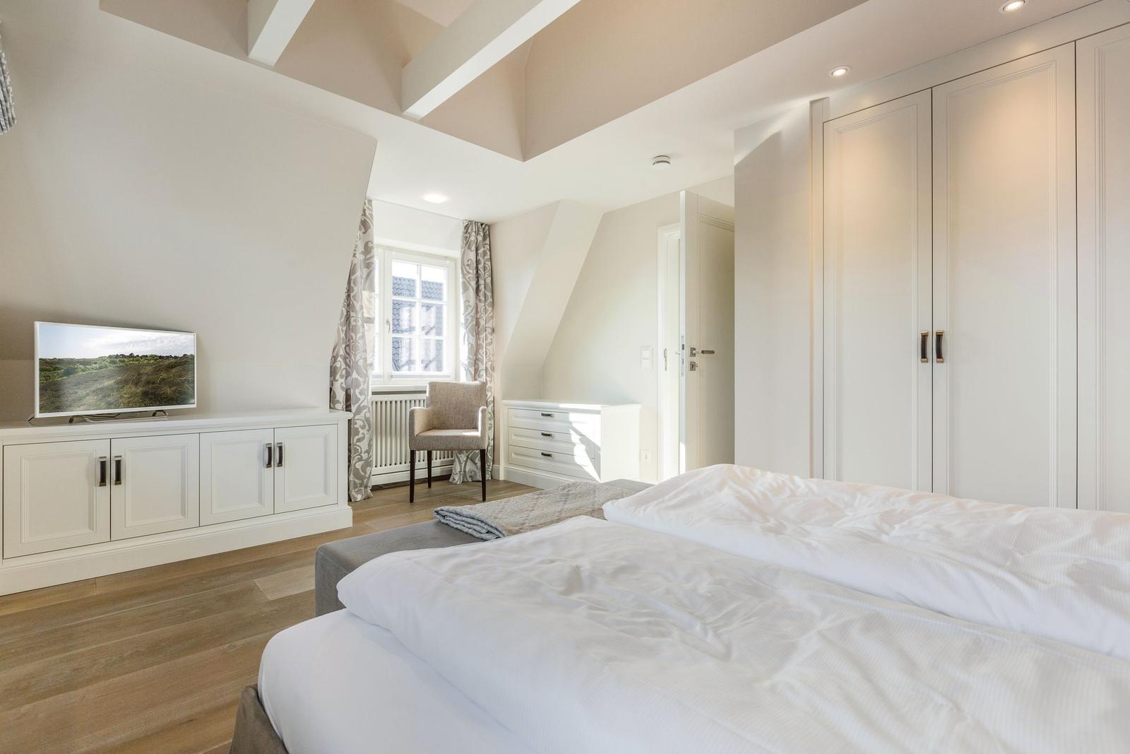 Schlafzimmer mit Doppelbett, Kleiderschrank und TV auf Sideboard.