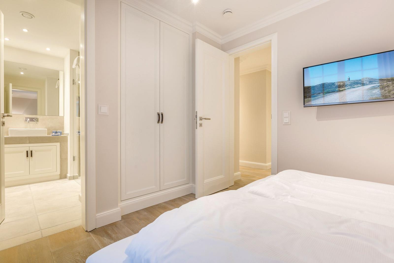 Schlafzimmer mit Bett, Kleiderschrank und TV. Badezimmer ist angebaut.