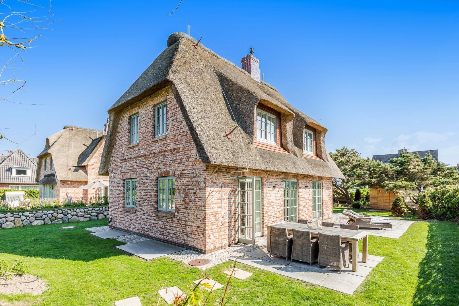Rotes Backsteinhaus mit Strohdach und Garten mit Terrasse.