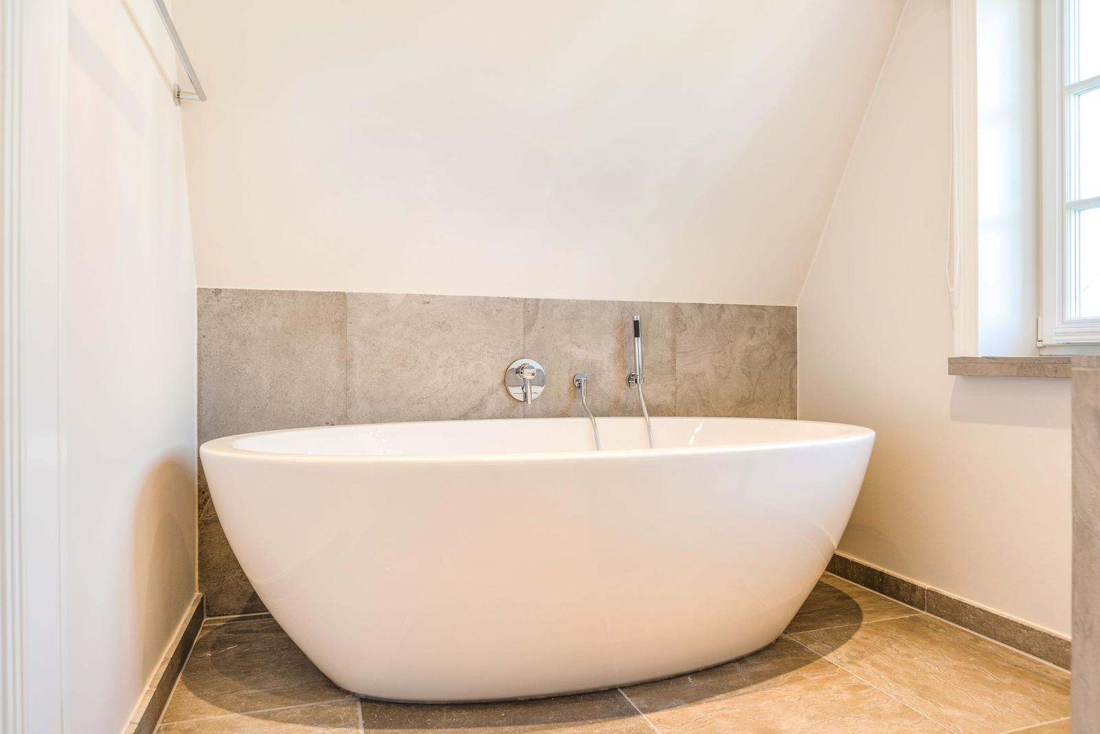 Freistehende Badewanne in Dachschrägen-Badezimmer mit Steinwand und Fenster