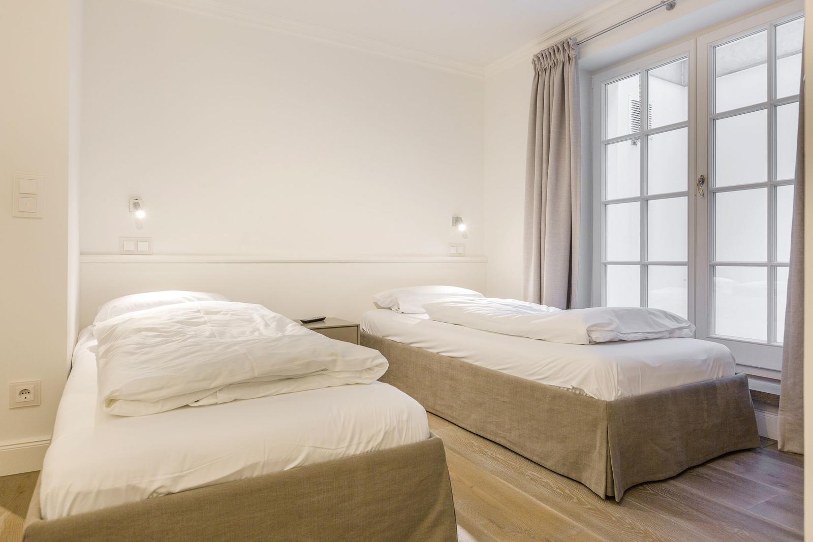 Zwei Betten mit weißen Bettwäschen und Holzboden. Fenster mit Vorhängen.