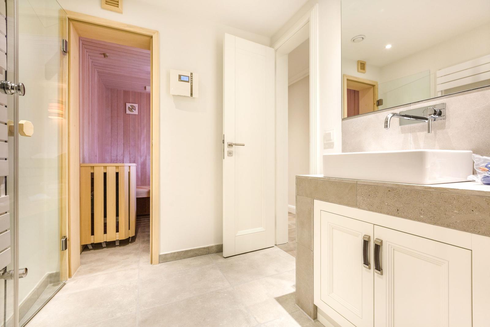 Badezimmer mit Dusche, Waschtisch und Sauna im Hintergrund.