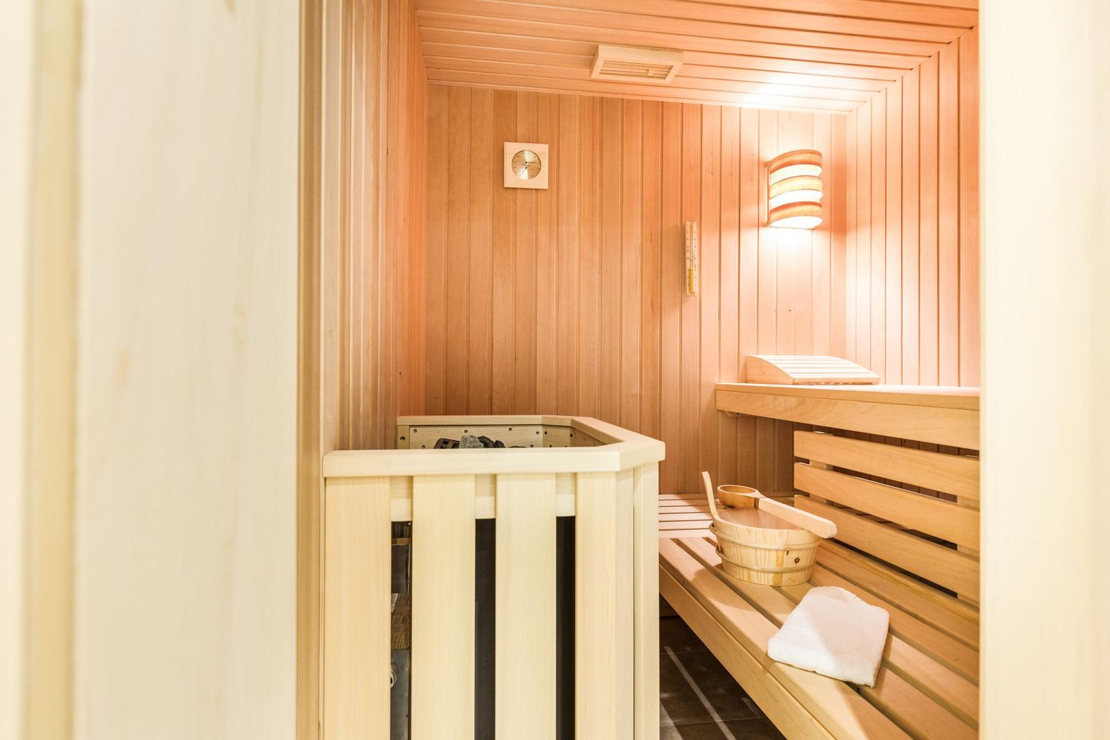 Sauna mit Holzbank, Holzwanne und Thermometer an der Wand.
