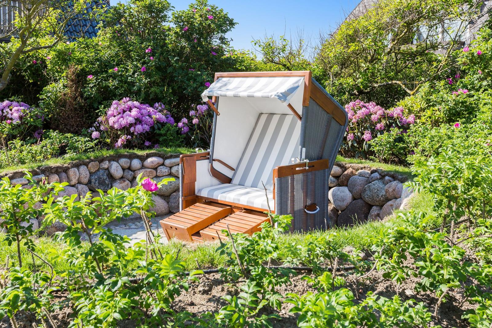 Strandkörbe mit Streifenbezug stehen im Garten mit Blumen und Steinmauer.