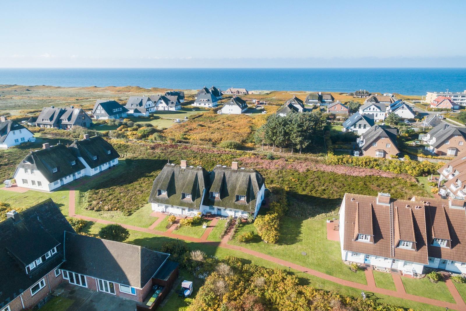 Aerielansicht von Häusern am Meer mit Grünflächen und Wegen.