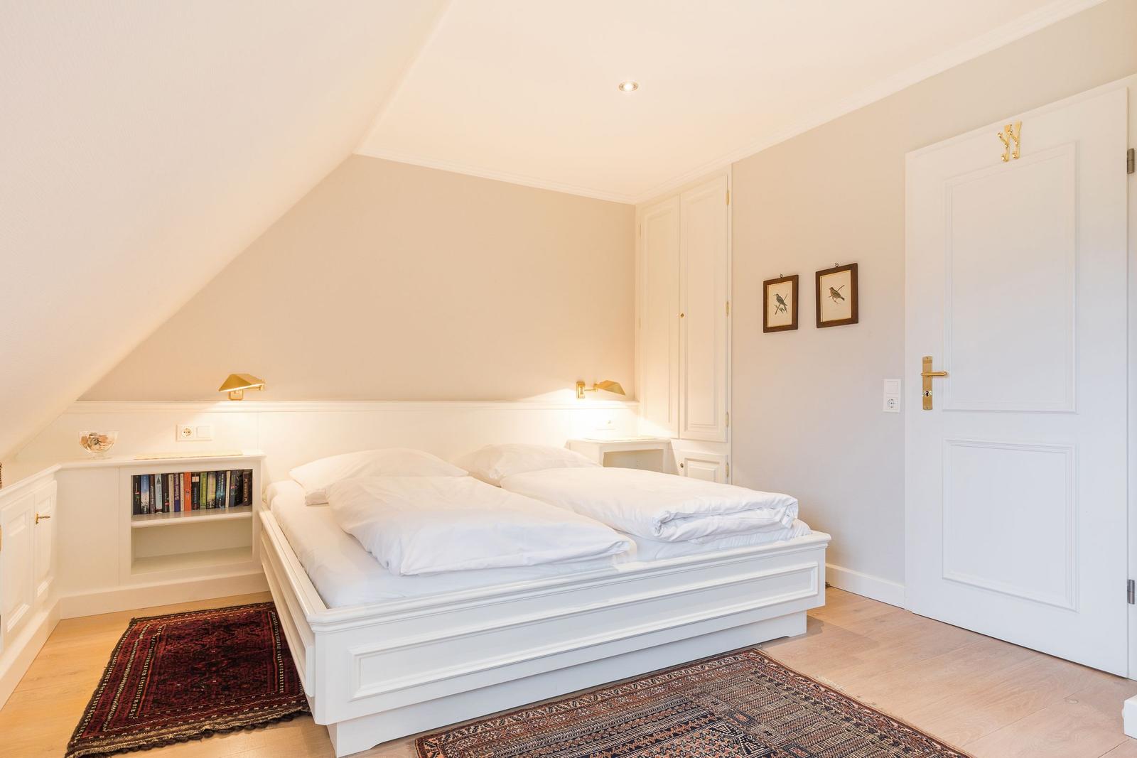 Schlafzimmer mit Doppelbett, Bücherregal und Tür.