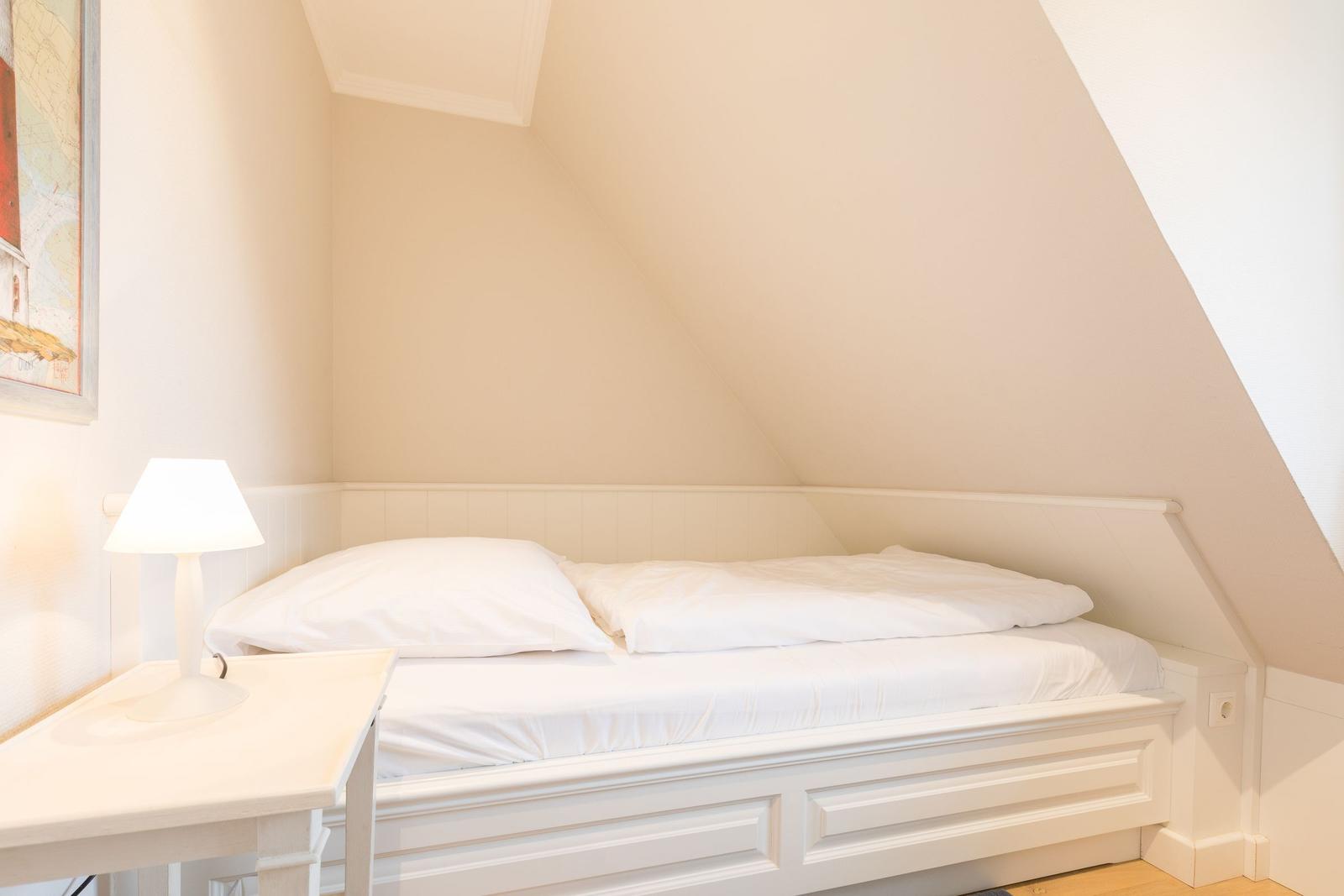 Ein Bett unter Dachschrägen mit weißer Bettwäsche und Nachttisch.